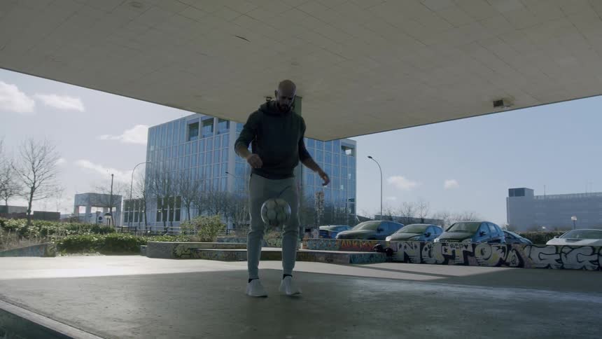 A man juggling football under a shade at midday