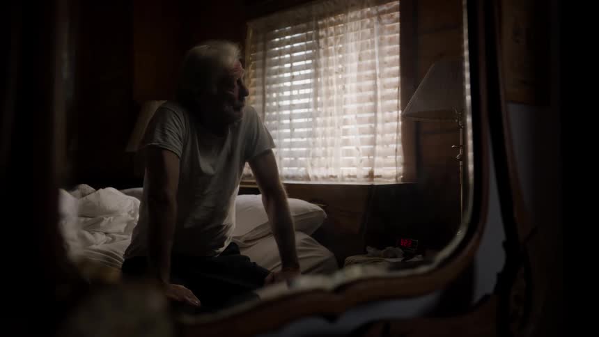 Elderly man sleeping and then waking up sitting on the bed and turning on the lamp next to him