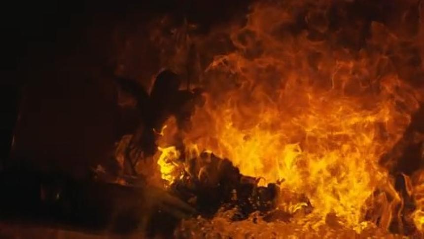 Burning desk and items on it collapse before a spray of water flows across flames and onto the charred desk