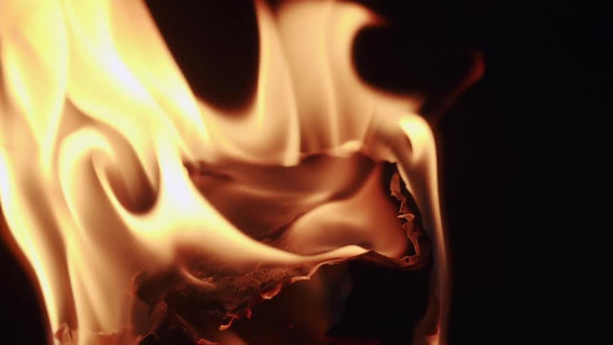 Orange flames and smoke rise from charring material in dark area