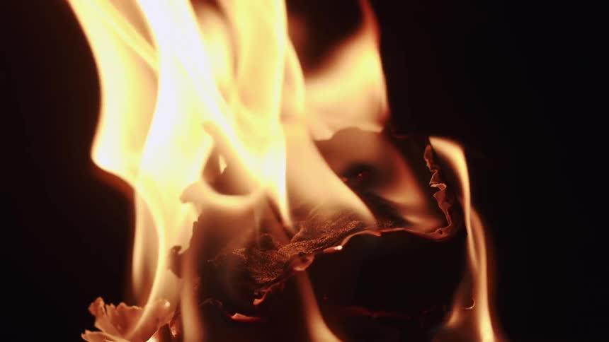 Flames rise from quickly charring layered object in darkness
