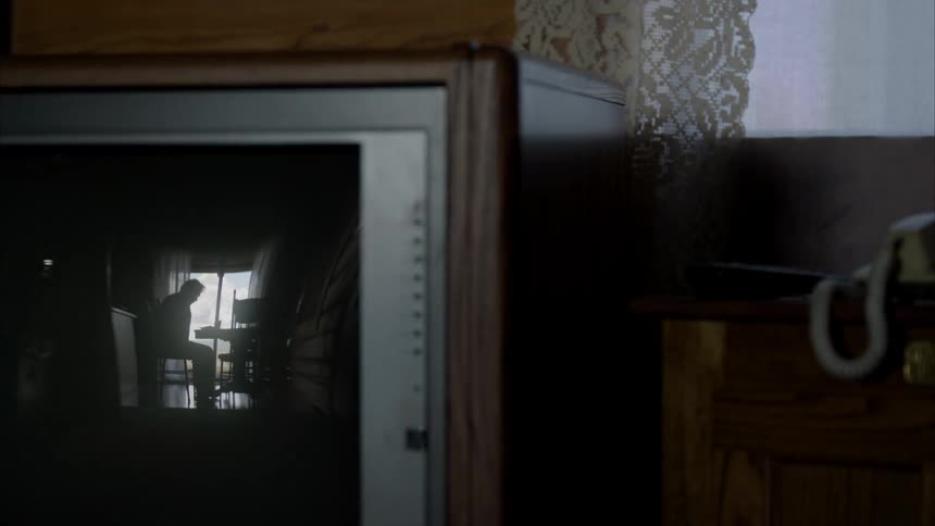 A black television with the screen off is reflecting a person sitting in a chair