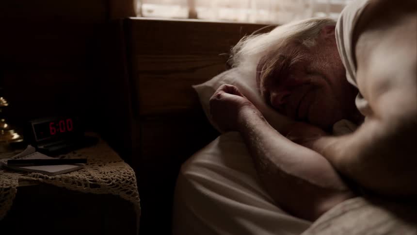 A man sleeps in bed when an alarm on his dresser wakes him