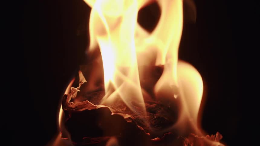 Closeup on a paper on fire with flames rising in slow motion