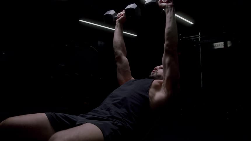 Man in a gym chair performing chest exercise lifting dumbbells upward