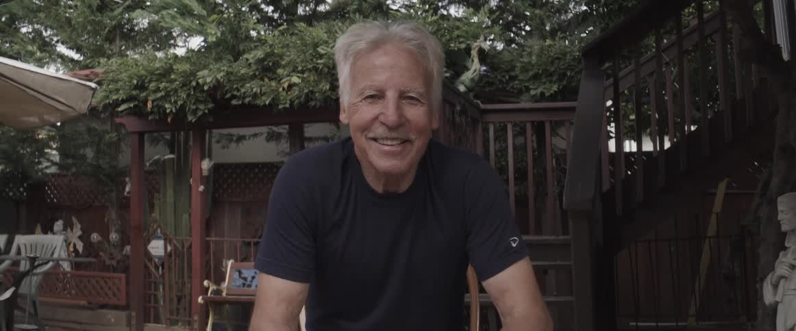 A smiling man sitting on a chair in the backyard