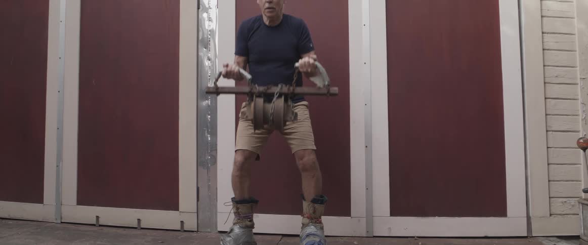 Elderly man wearing makeshift shoes in the backyard lifting weights