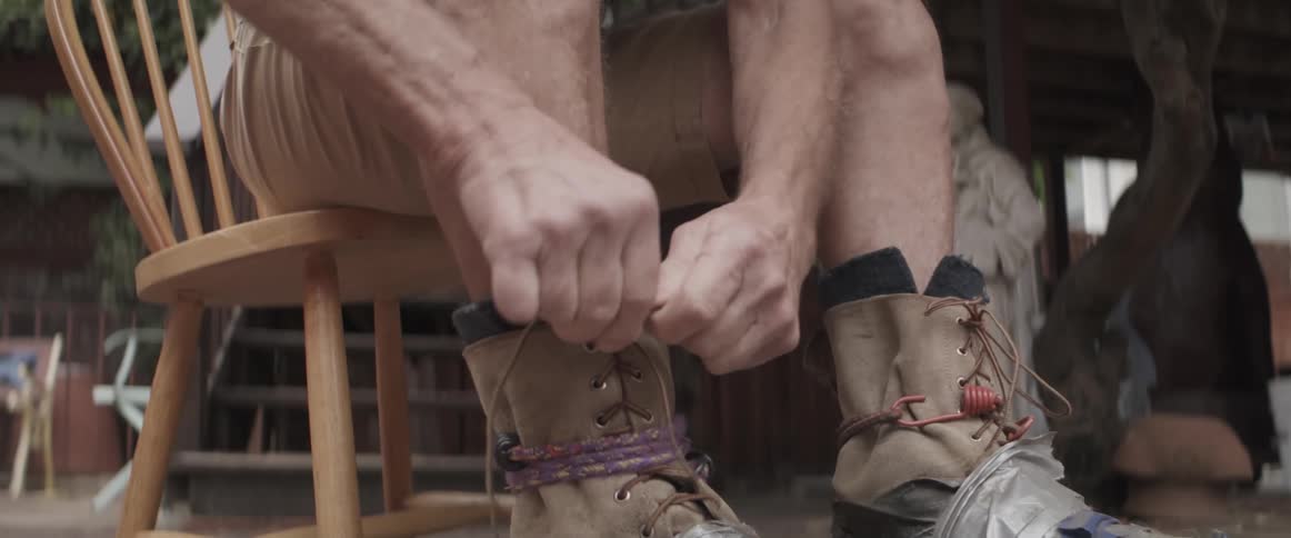 A seated person is tying the laces of a boot that is covered in duct tape