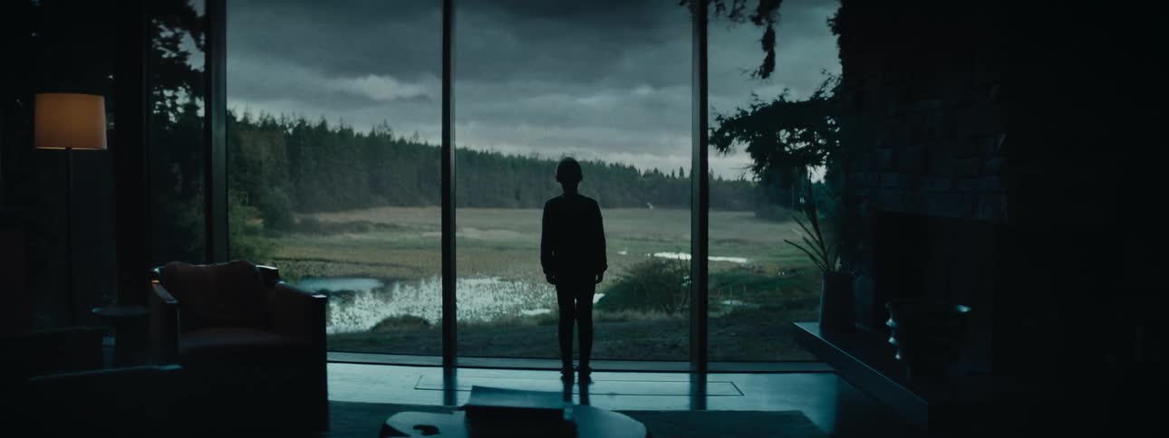 A young woman looking out large modern windows at a storm