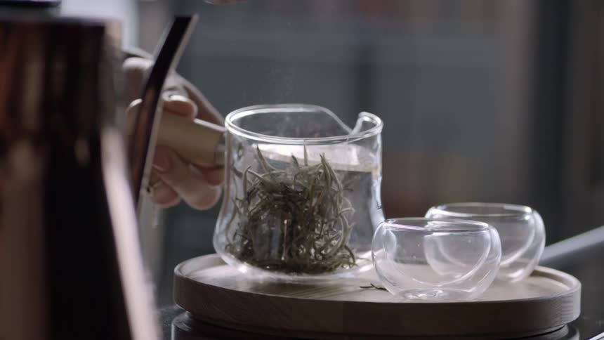 A human hand placing plants that are in a bowl into a clear glass jar