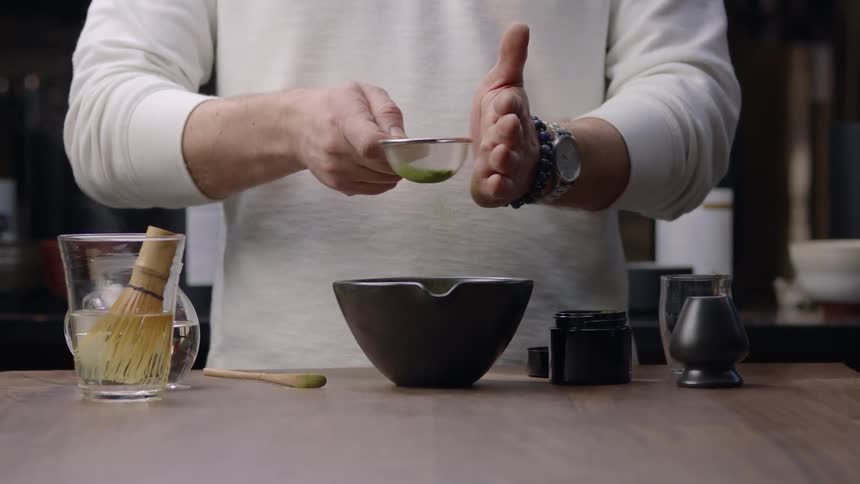 A person is using a sieve to sift a green object and is hitting the sieve in his hand