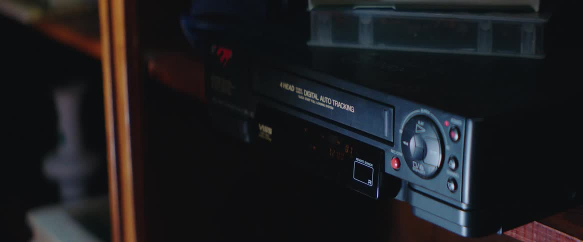 A pair of hands inserts a cassette tape into a vcr
