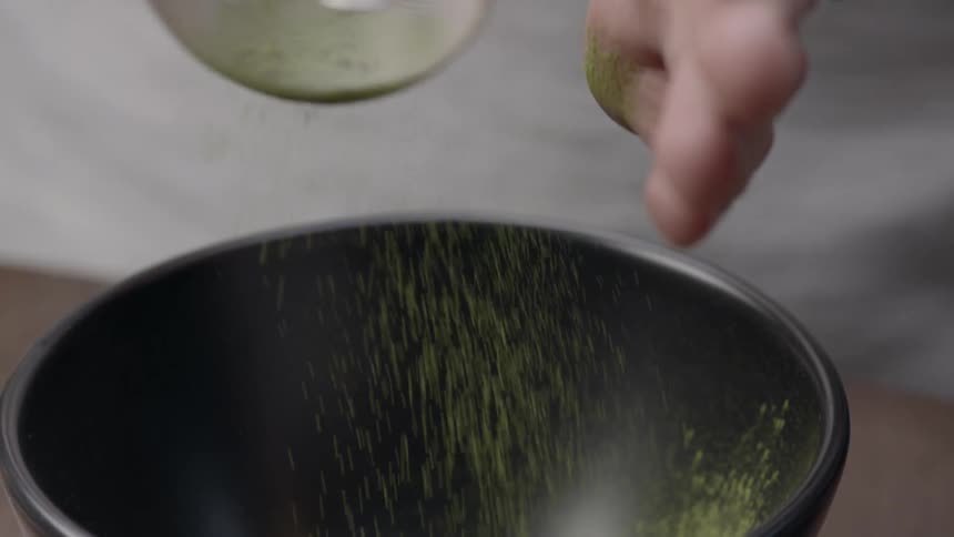 A person sifts a substance into a bowl