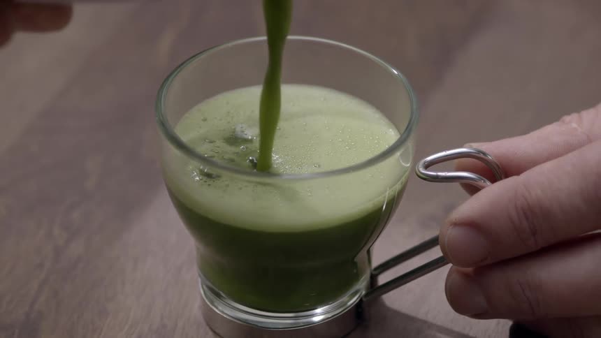 A green foamy drink is poured from a bowl to a coffee cup