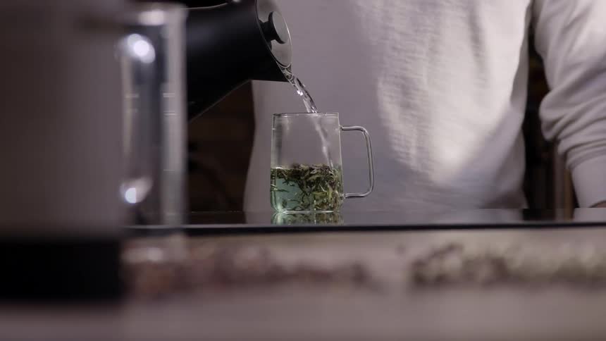 Hands of a man pouring hot water into a glass cup with herbs