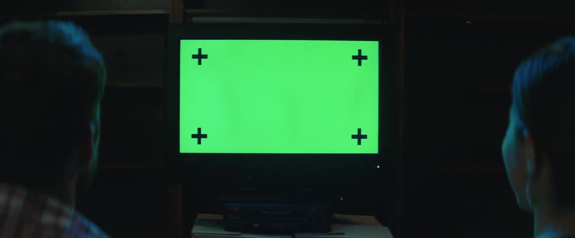 Two people watch a green pattern on a television and laugh