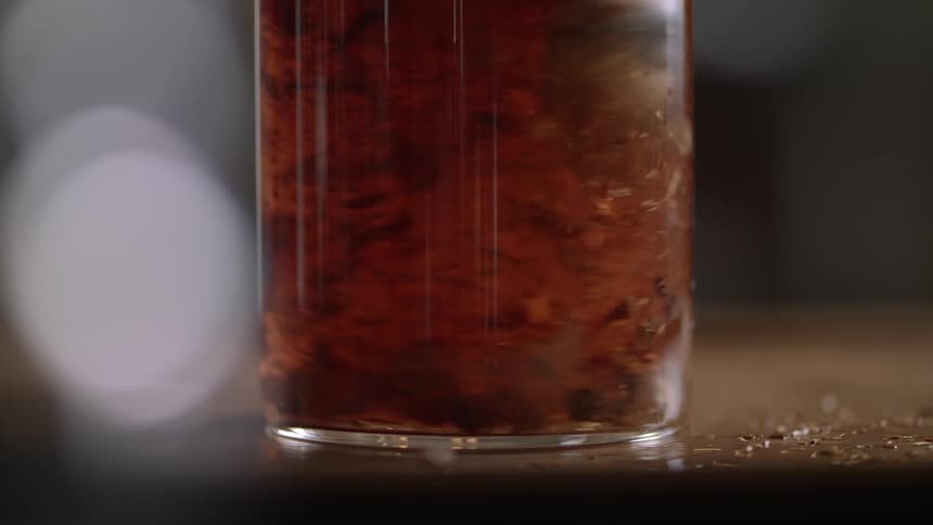 A spoon stirring inside a glass with a liquid filled with red elements