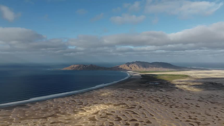Ocean waves foaming on a curved sandy beach on a peninsula