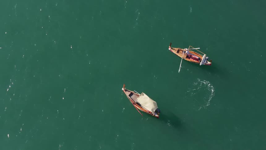 Two small wooden boats traveling in the middle of a greenish sea