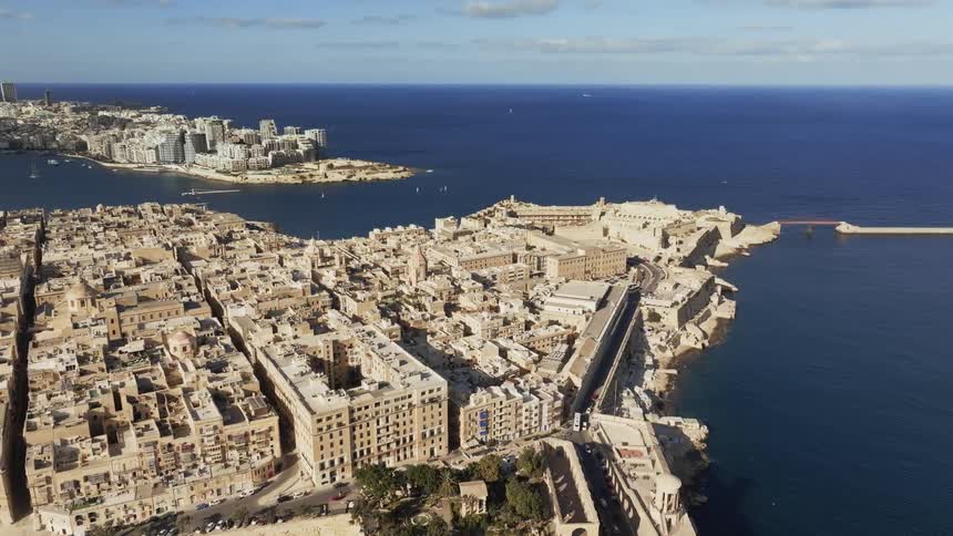 City buildings densely cover land bordering water on both sides of harbor under a cloudy sky