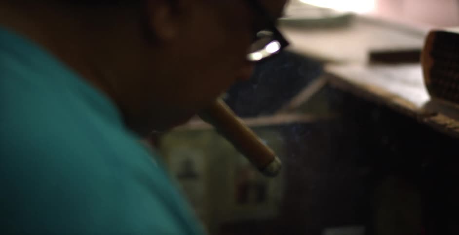 A man smoking a cigar works on rolling a cigar in his hands
