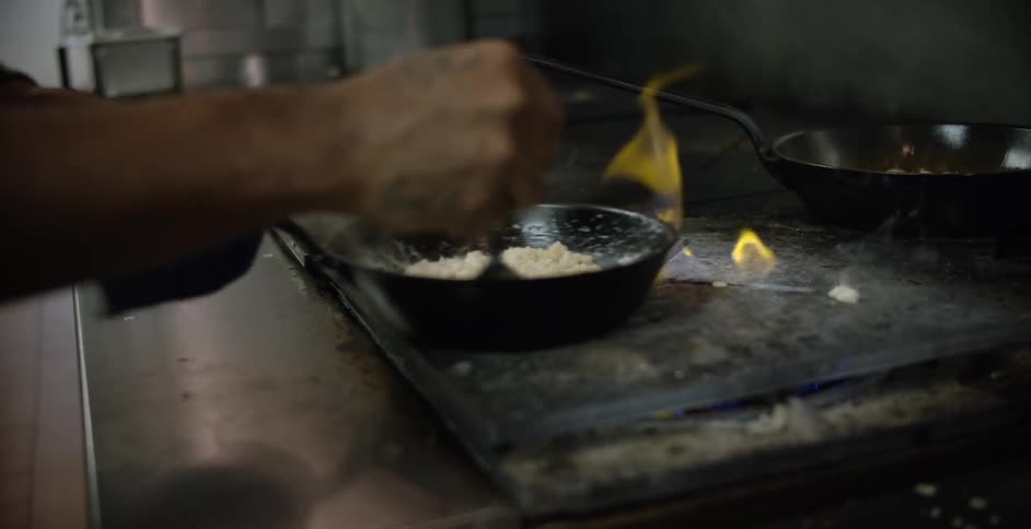 A chef cooking food in a pan over a flame