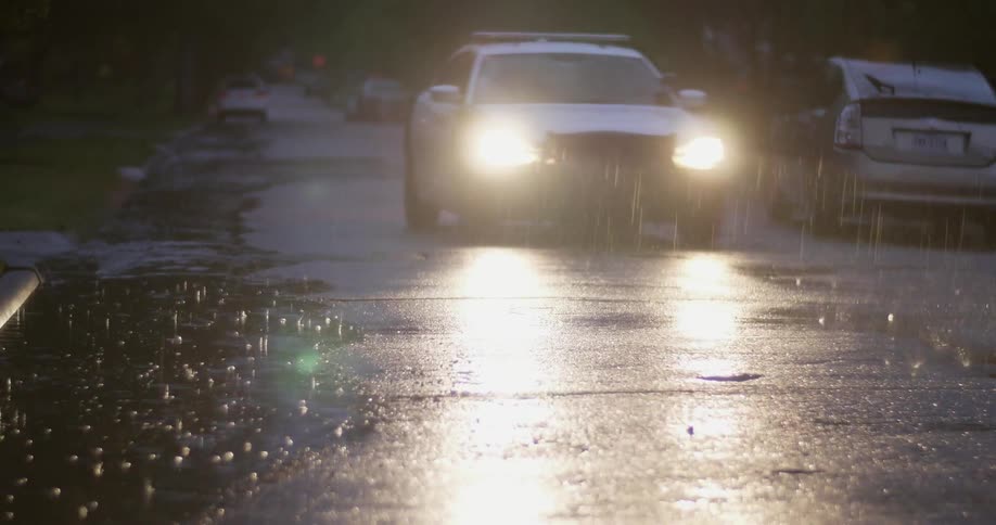 A neighborhood street in the rain as a car drives past