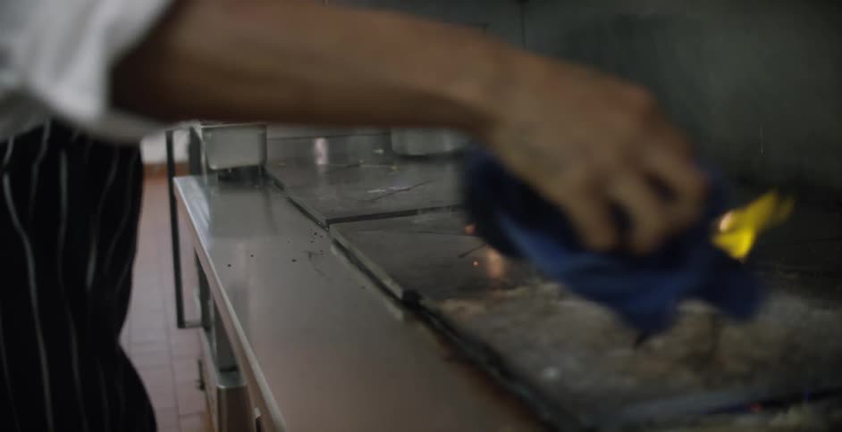 A chef wiping down a stove as it is still flaming