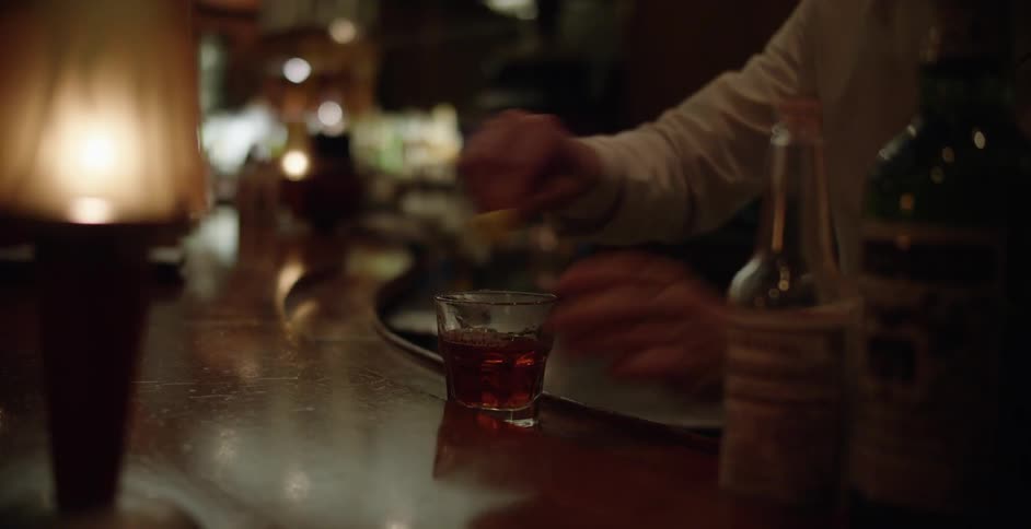 A man at a bar rubbing lemon around the rim of a drink