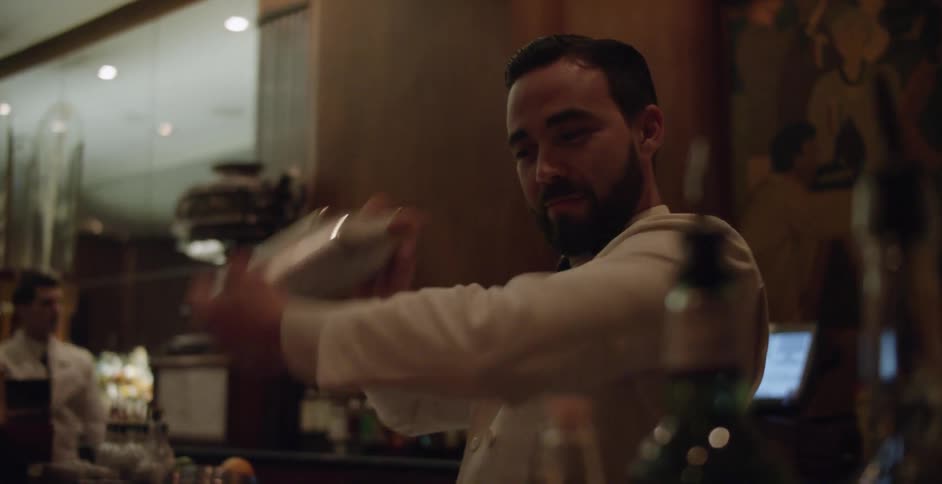 A bartender mixes a drink in a steel shaker