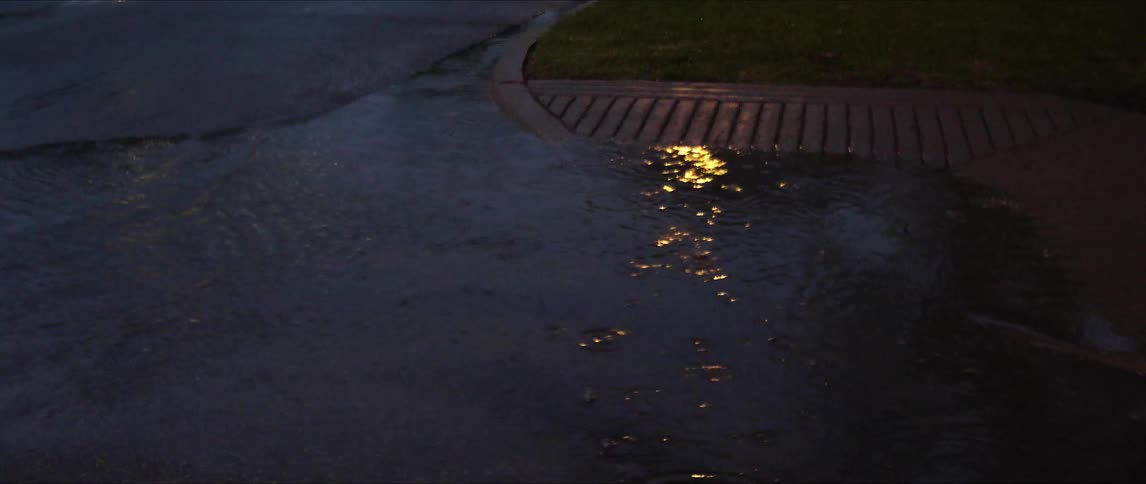Rain is causing a large puddle near the sidewalk at night