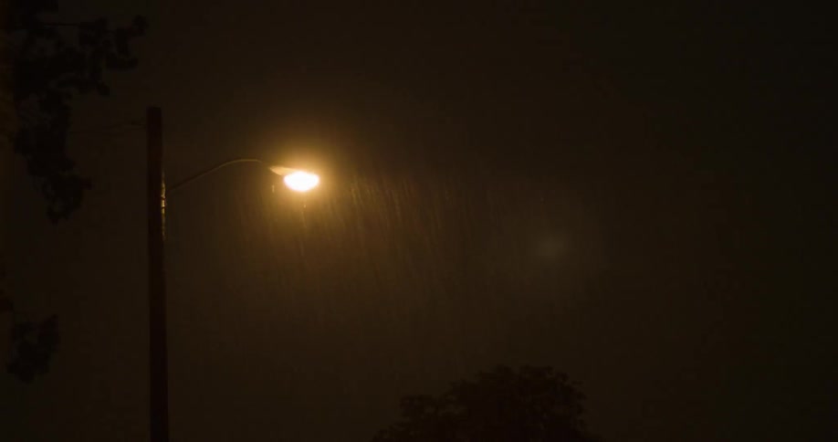 A lit street lamp has rain falling around it