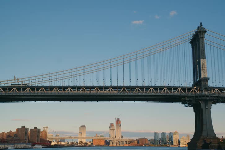 Traffic moves across a suspension bridge spanning a river near a city