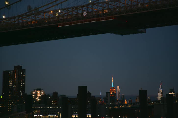 Vehicles crossing bridge with city skyline in the background at night