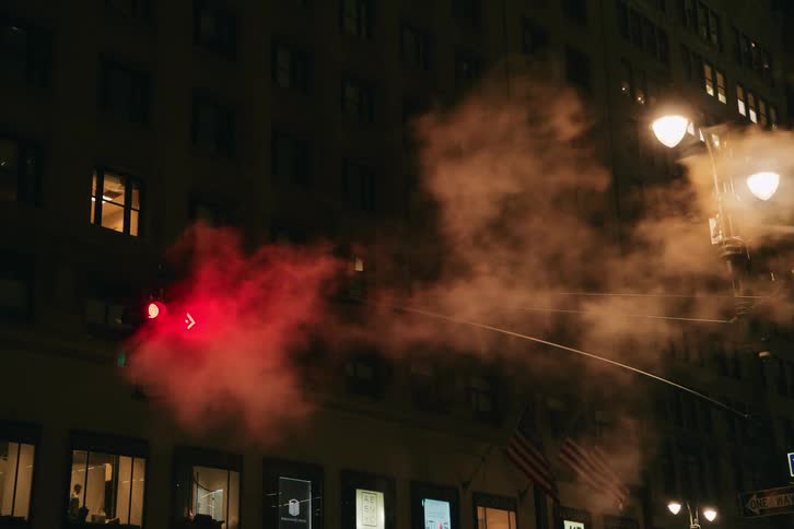 External view of a traffic light at night in a metropolis with smoke passing by