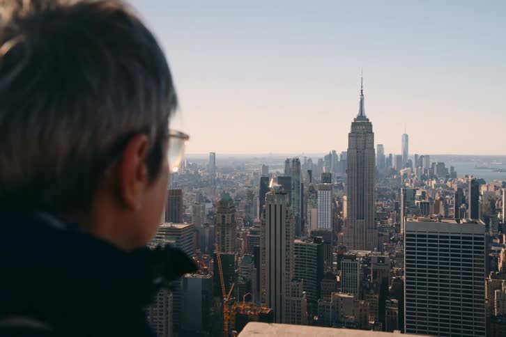 A man looking outdoor at city skyline while standing indoor during the day