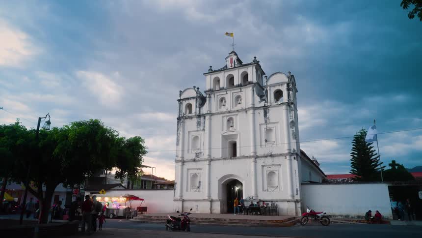 A white building that looks like a spanish style mission has people standing nearby