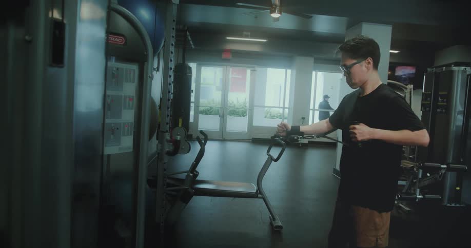 A teen working out with the cable machine inside the gym at midday