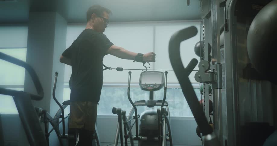 A teenager working out using the cable machine in a gym at midday