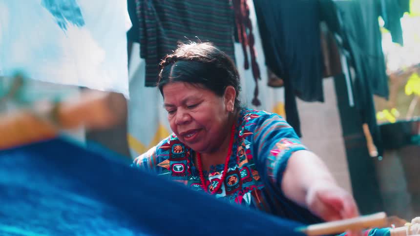 An indigenous woman making clothes with blue fabric