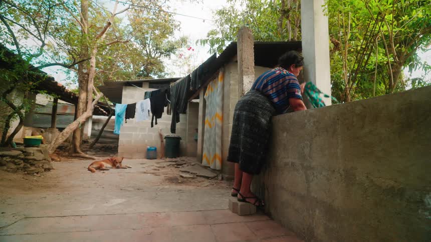 Woman stands on stone block while hand washing clothes in paved yard