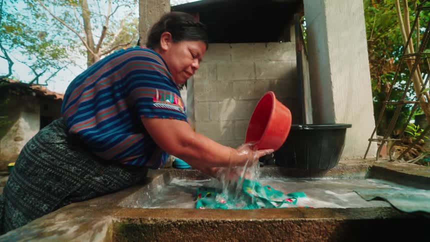Smallsized woman scooping water and pouring it onto a tshirt while washing her hands