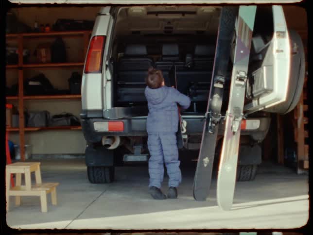 A child loads snow skis into an suvs trunk in a garage