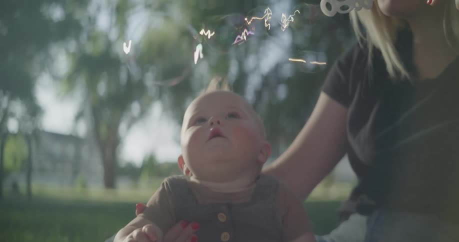 A mother blowing soap bubbles for her baby in a park