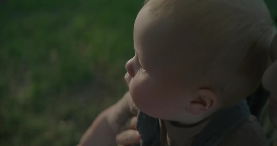 Mother holds her baby standing on green lawn