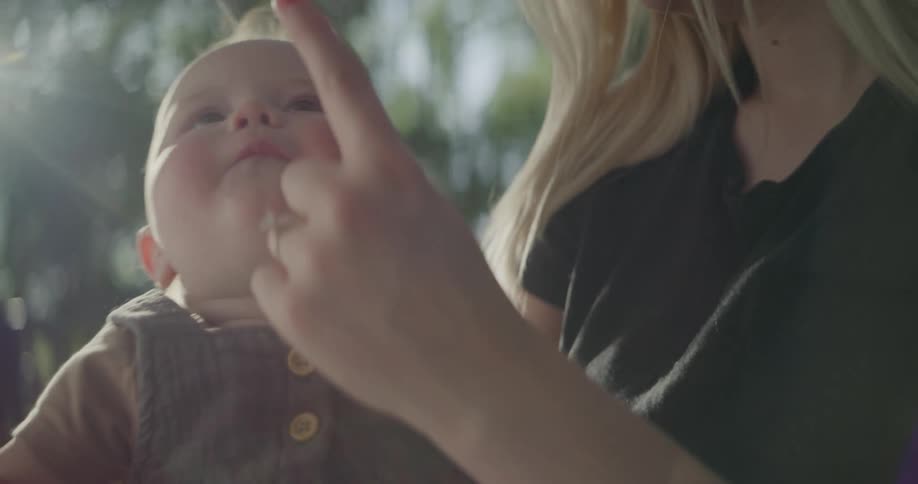 A baby plays with its mothers fingers in a park during the day