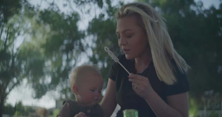 A woman having a picnic with a baby blows soap bubbles to entertain the child
