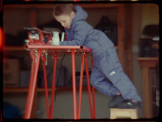Little boy in the garage leaning on a table with a machine