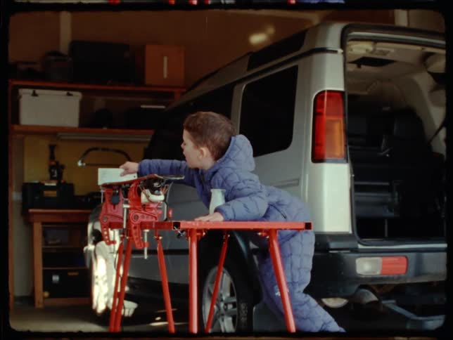 Little boy in the garage at home playing with scraping an object on a machine on the table