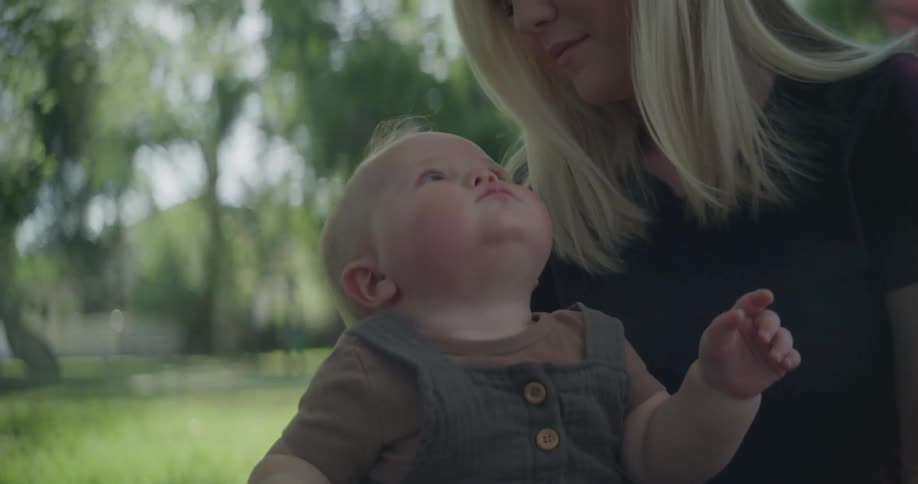A blonde haired woman sits outdoors with a young baby